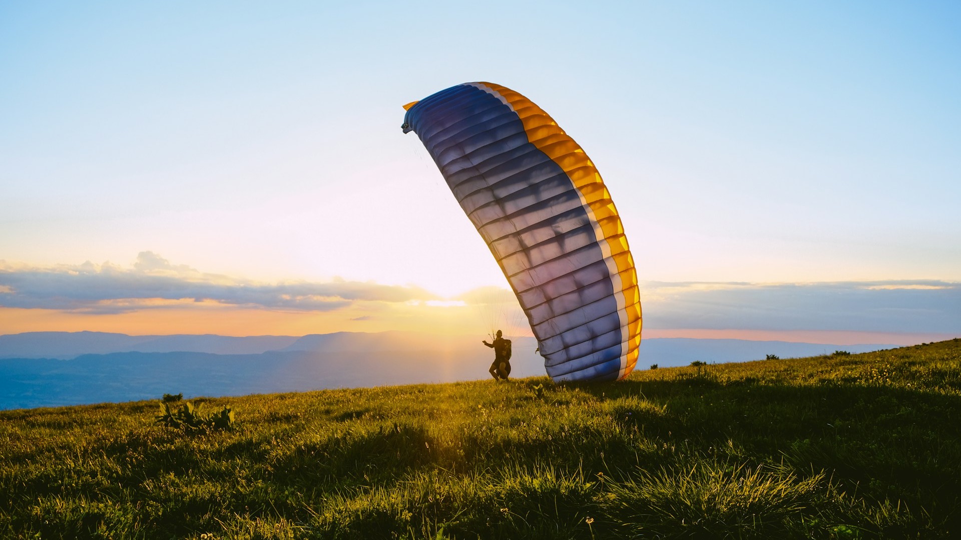 Gleitschirmflieger startet bei Sonnenuntergang vor Bergpanorama